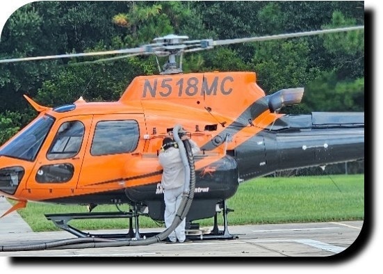 An orange helicopter on a helipad, refueling by a person in protective gear with a hose connected to the helicopter.