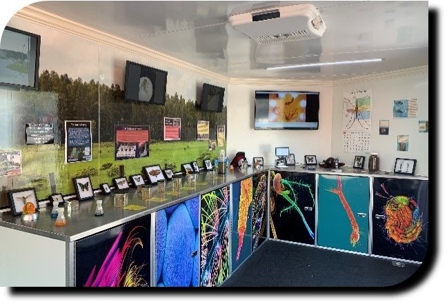 Interior of a room with a counter displaying products, informational graphics on the walls, and a TV screen.