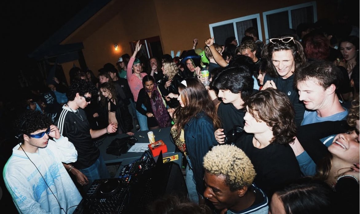 A lively gathering at a party with people dancing and enjoying music, featuring a DJ and a vibrant atmosphere.