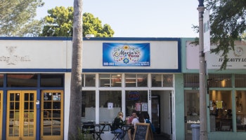 A colorful storefront with a sign, featuring outdoor seating and people sitting at tables.