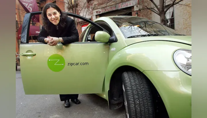 A woman leans on the open door of a green Zipcar, promoting car-sharing services in an urban setting.