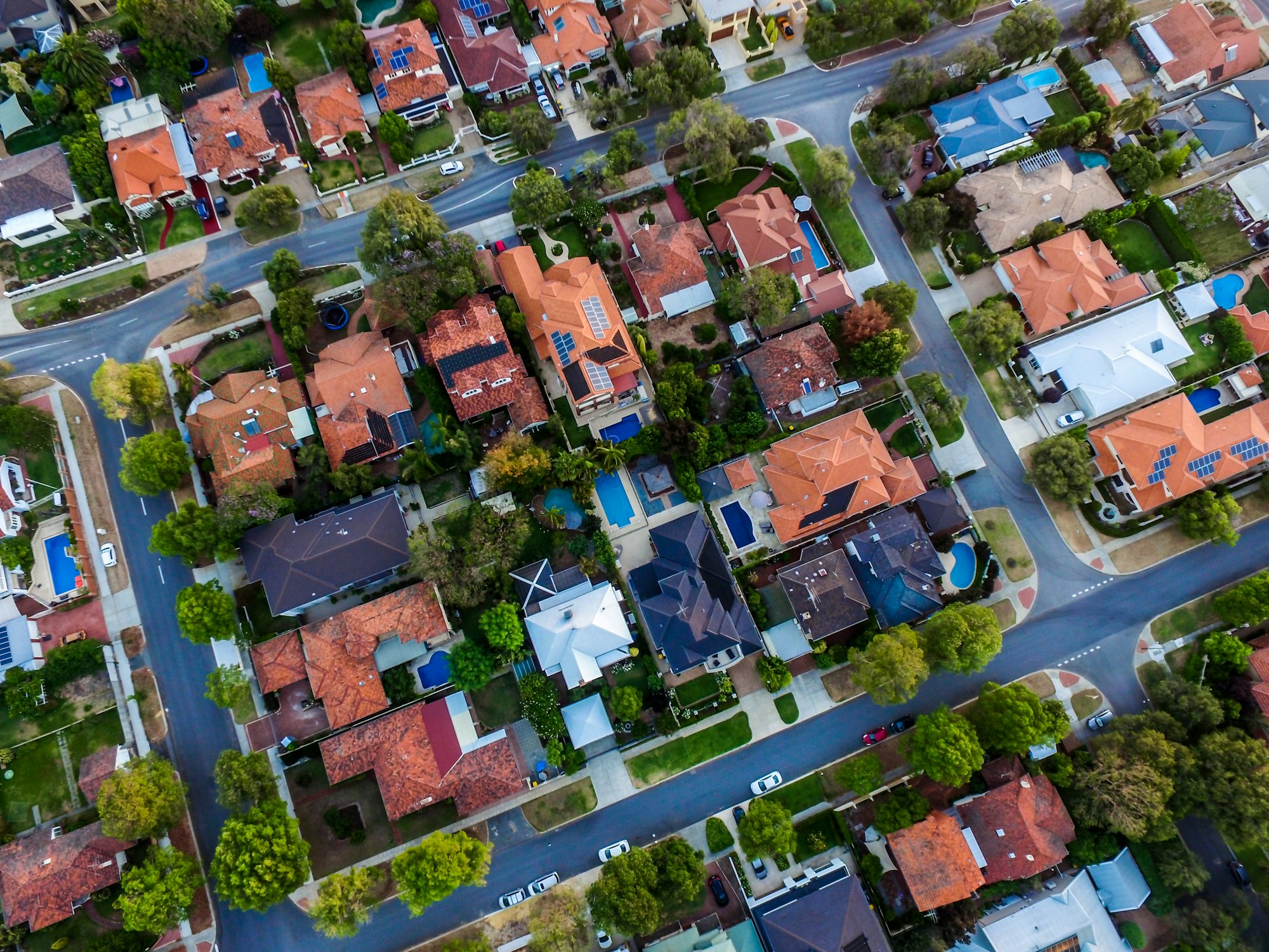 An aerial view of a residential neighborhood with houses, rooftops, trees, and a few swimming pools visible.