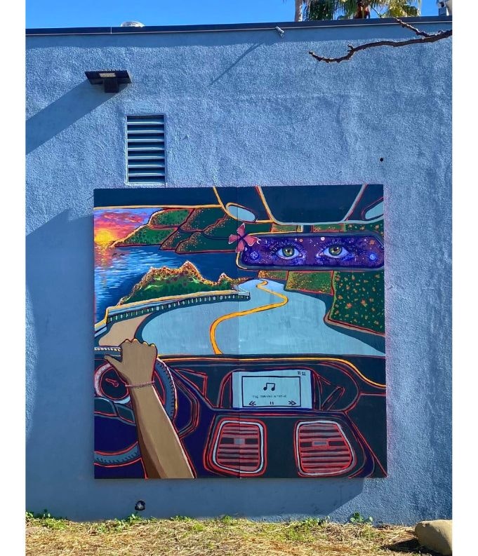 A colorful mural showing a hand on a car steering wheel, a scenic road on the dashboard, and eyes in the rearview mirror.
