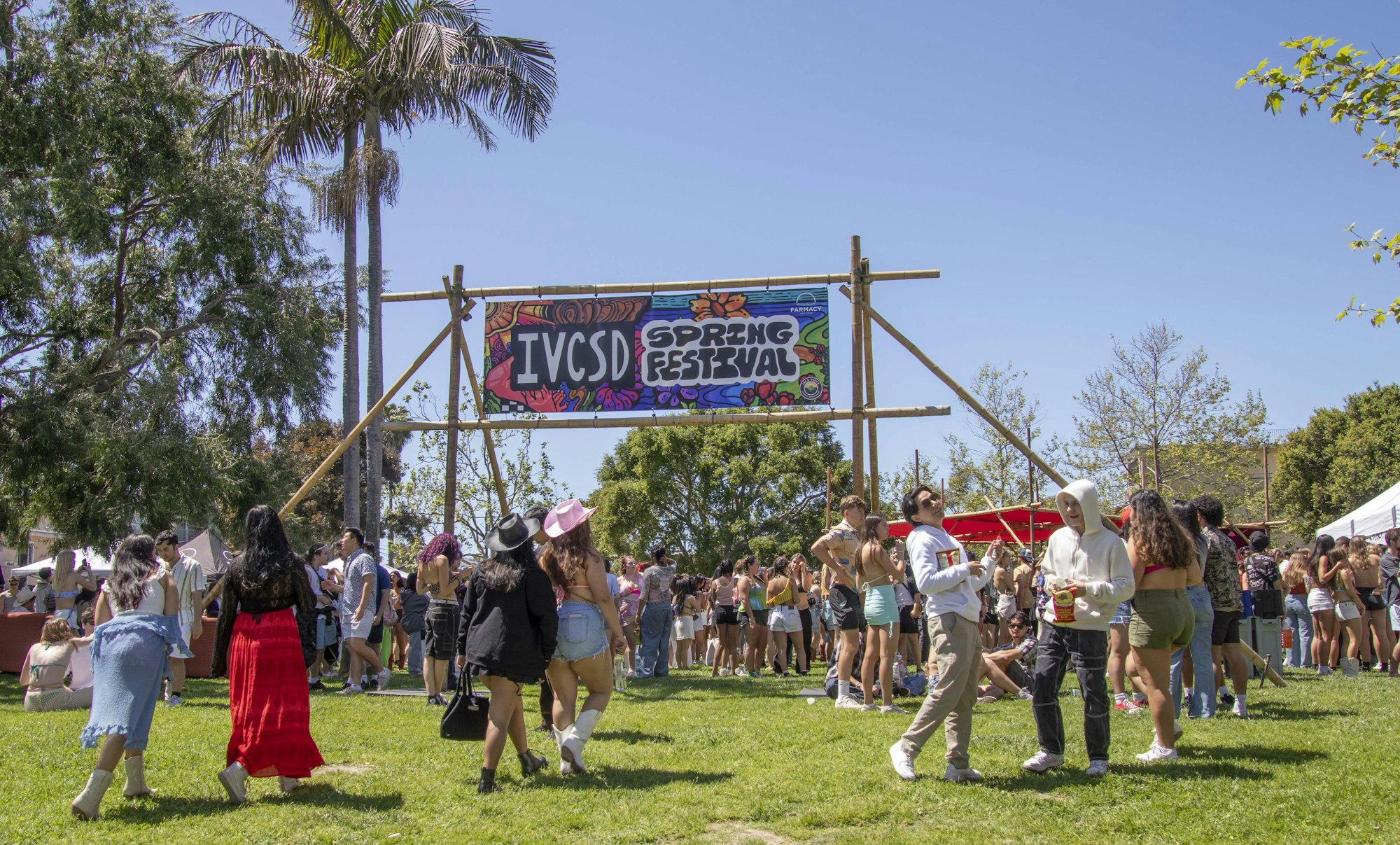 Outdoor spring festival with people socializing, a clear sky, and a sign indicating the event.