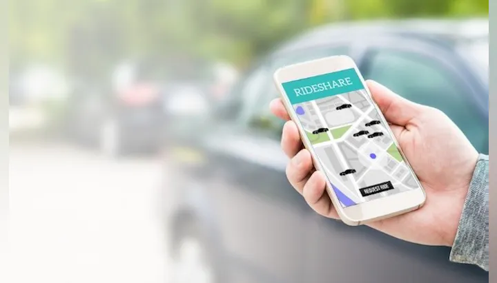 A person holding a smartphone displaying a rideshare app map with car icons, indicating nearby rides.