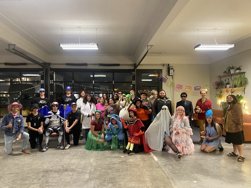 A group of people in various costumes posing for a photo in a room with festive decorations.