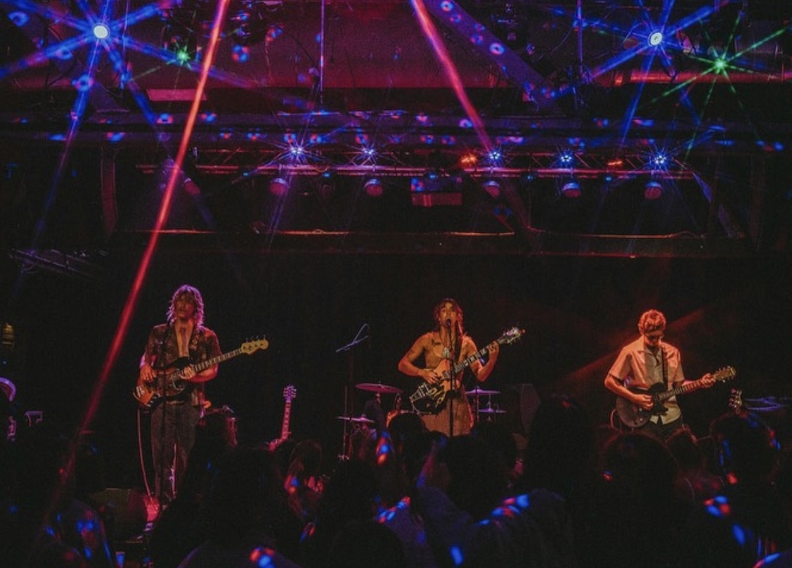 A lively band performs on stage with colorful lights and an energetic audience enjoying the music.