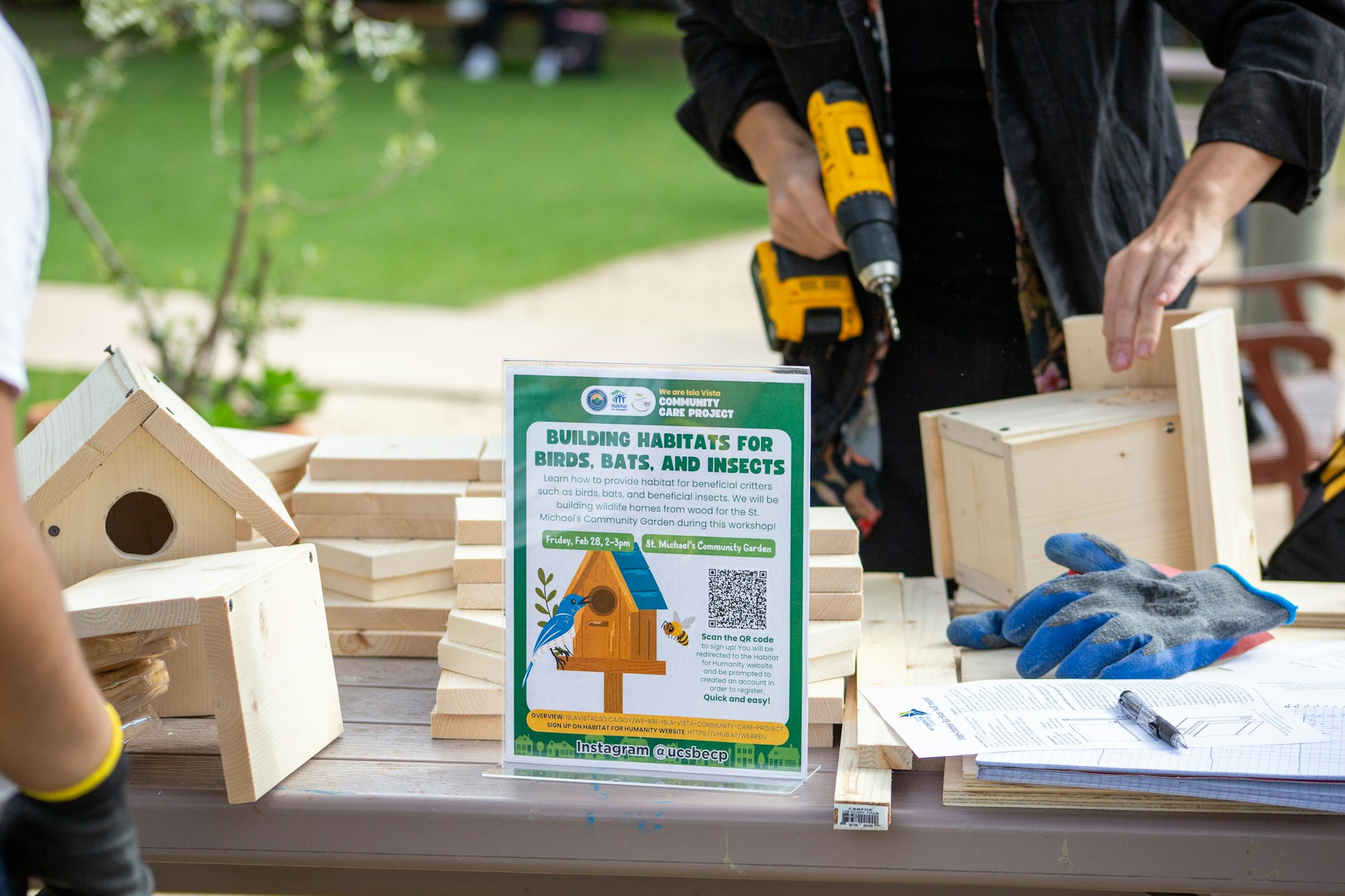 People building wooden habitats for birds, bats, and insects at a community workshop, using tools and wood pieces.