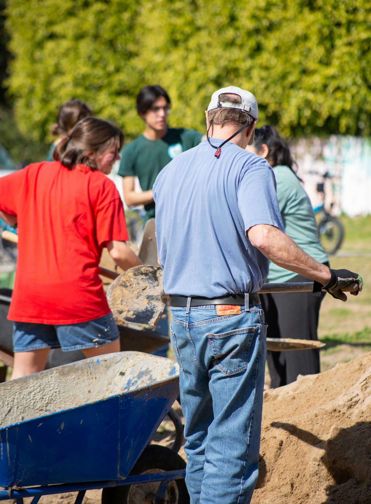A group of people working together with shovels and wheelbarrows, possibly doing outdoor construction or gardening tasks.