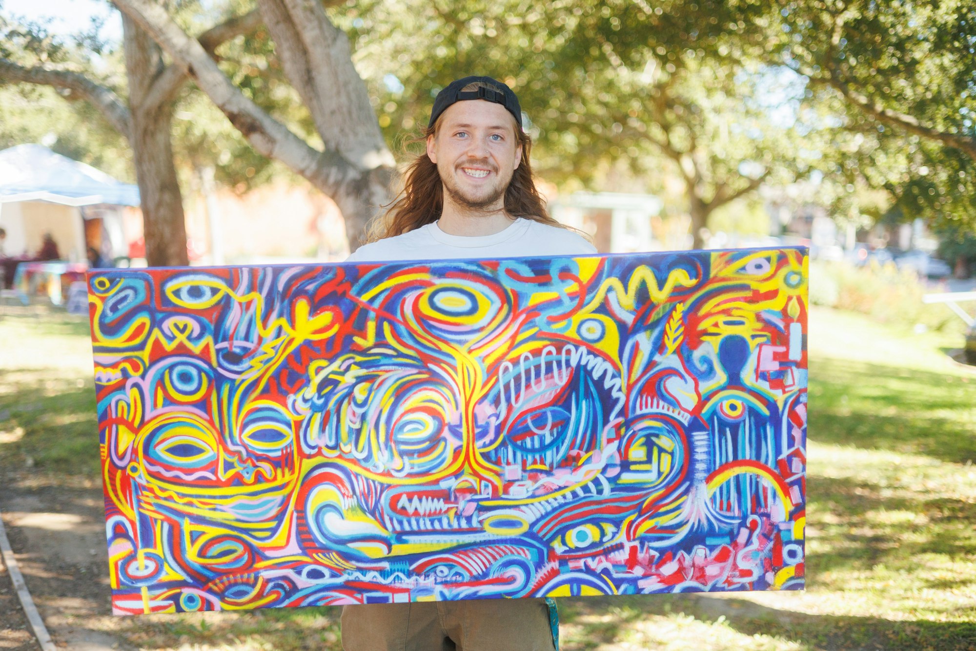 A person holding a colorful abstract painting outdoors.
