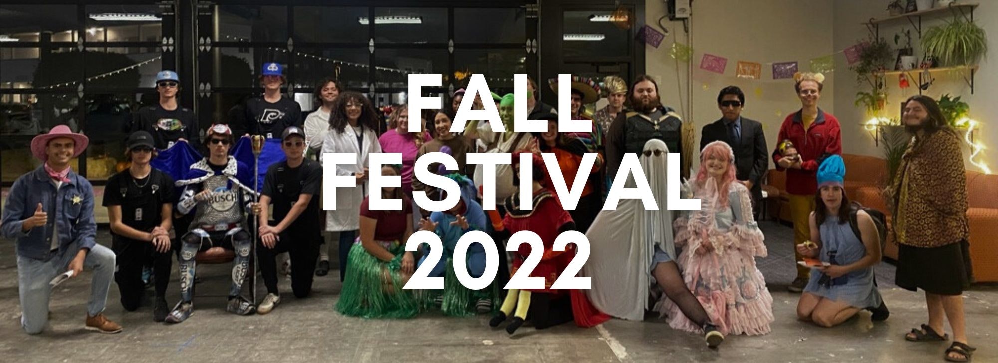 A group of people in various costumes posing for a photo at a "FALL FESTIVAL 2022" event.