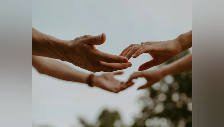 Two hands reaching out to each other, one with a ring.