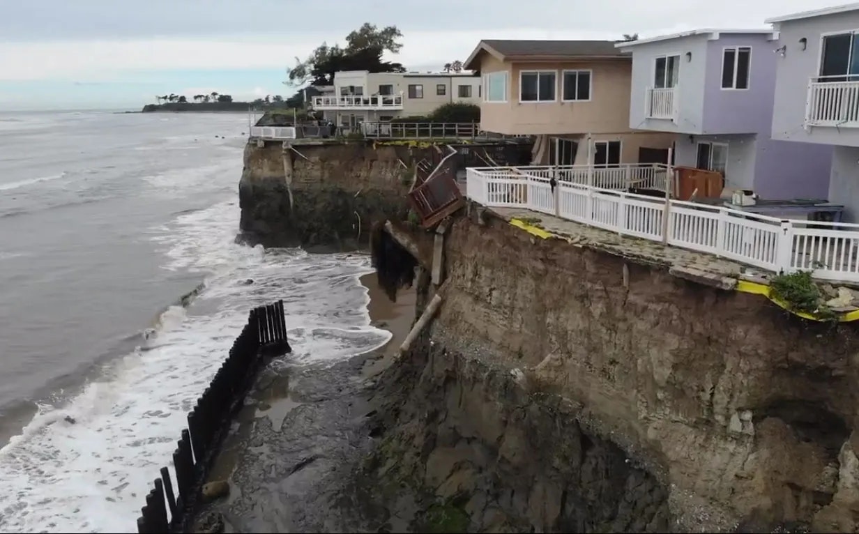 A coastal area with eroded cliffs threatening houses, showcasing the impact of erosion and possible structural damage.