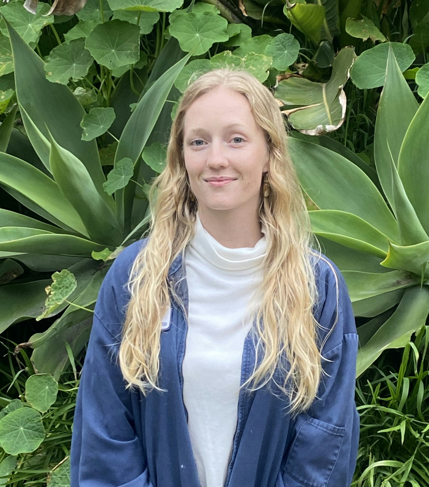 A woman with blonde hair in front of green foliage.