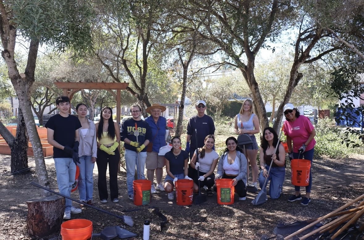 A group of people posing outdoors with tools and buckets in a park setting, suggesting a community or volunteer event.