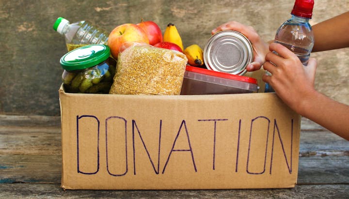 A food donation box with hands holding it, containing fruits, water, and non-perishables.