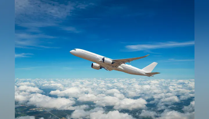 An airplane is climbing above a sea of clouds, under a bright blue sky with some wispy clouds.