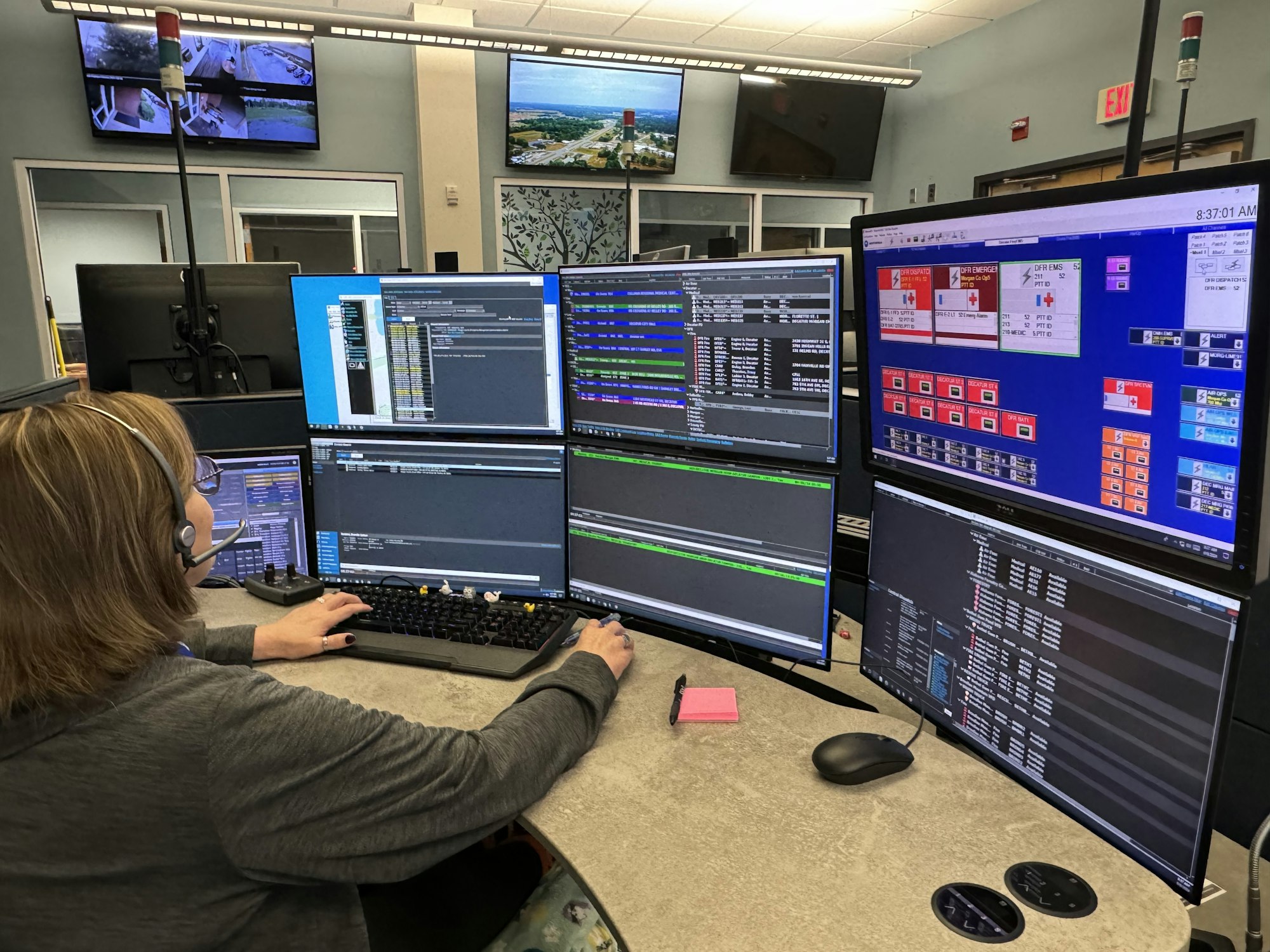 A person at a multi-monitor workstation with various applications open, possibly in a control room or office setting.