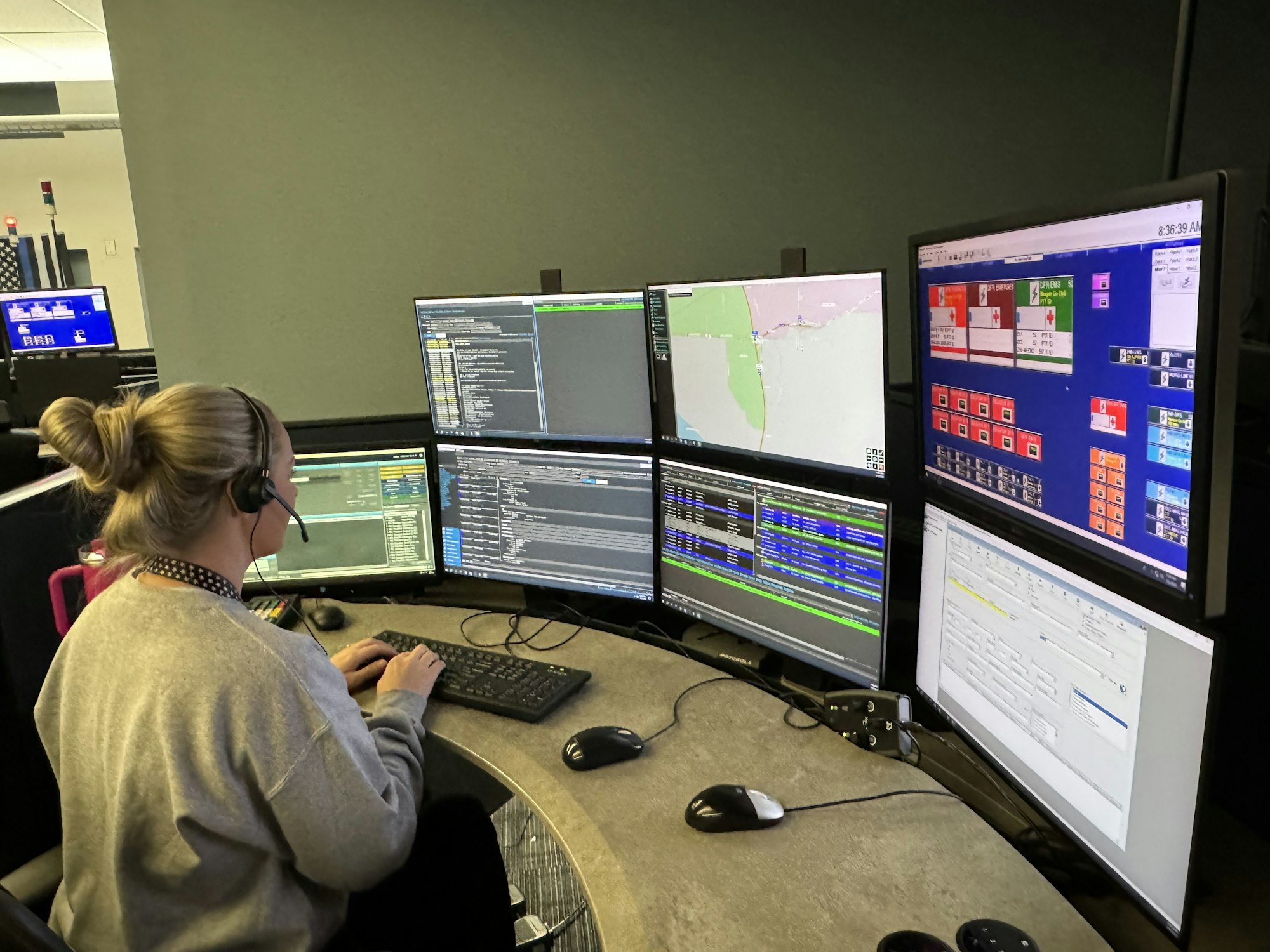 A person at a multi-monitor workstation with various data and map displays.