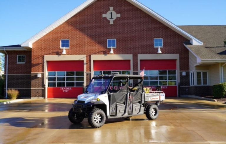 A utility vehicle parked in front of a fire station with red garage doors and a striking blue sky.
