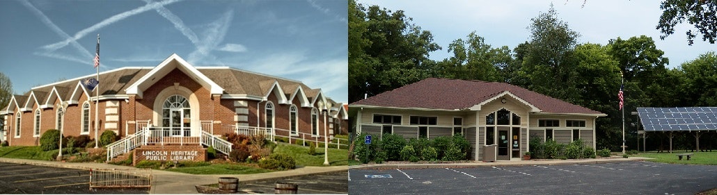 Two buildings: a brick library with an American flag and a smaller building with solar panels, set against trees.