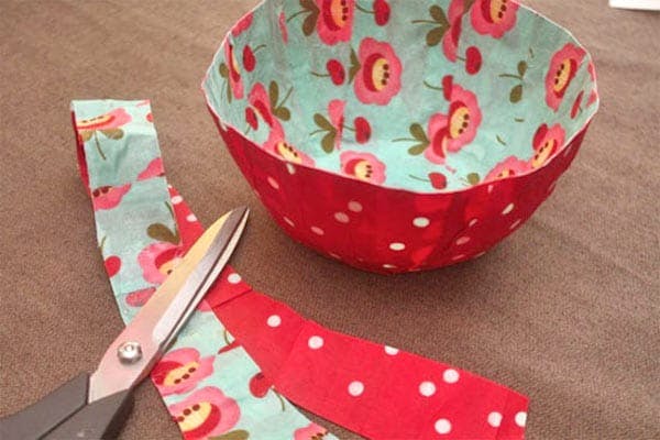 An image of a colorful, floral-patterned bowl and some cut fabric strips nearby, with scissors on a table.