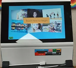 A touchscreen device interface with a "Touch here to begin" message and various photographs.