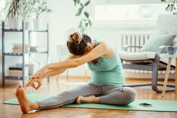 A person is doing a stretching exercise on a yoga mat in a bright, home-like setting.