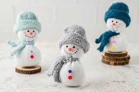 Three cute snowman figurines wearing colorful hats and scarves, set on wooden bases, with cheerful facial features.