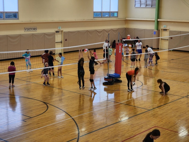 Indoor volleyball court with people playing and practicing.