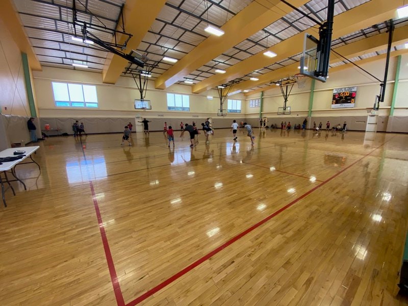 Indoor basketball court with players, hardwood floors, hoop, and scoreboard displaying 15:30 time.