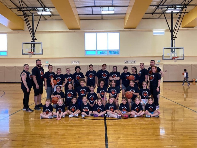 A group of children with coaches in a gym, wearing team t-shirts, posed for a group photo.