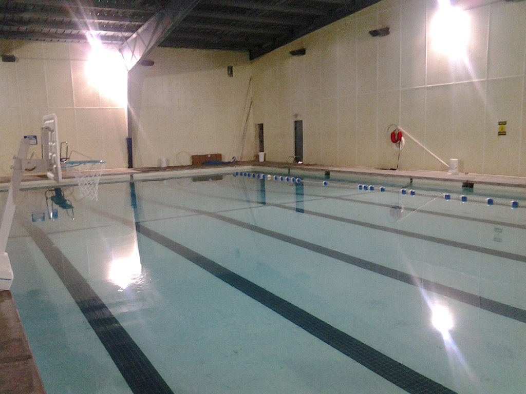 An indoor swimming pool with lanes, a basketball hoop, and lifebuoy, under artificial lighting.