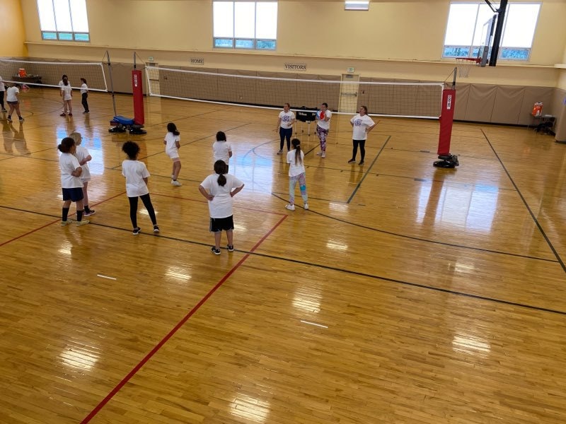 Indoor volleyball court with children practicing and a red volleyball net set up.