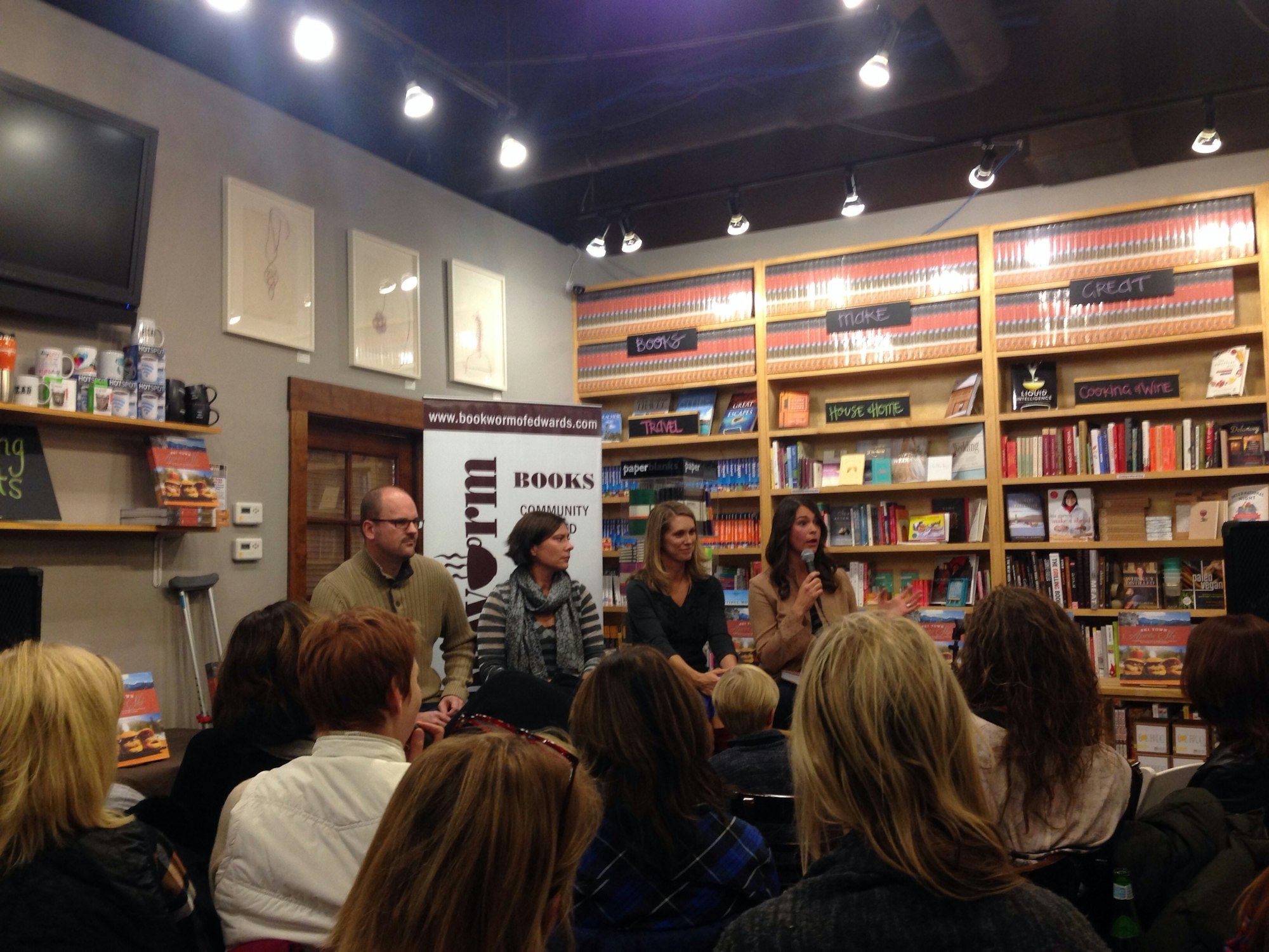 A group of people gathered in a bookstore with speakers at the front, likely at a book event or reading.