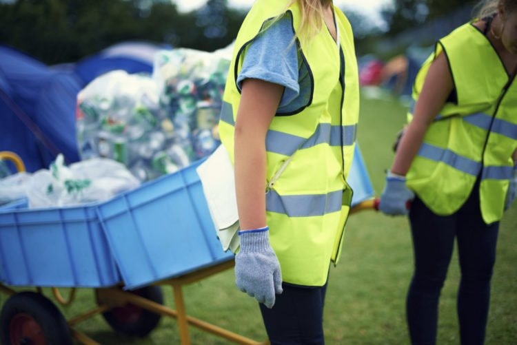 People in high visibility vests with a wheelbarrow full of recyclables.
