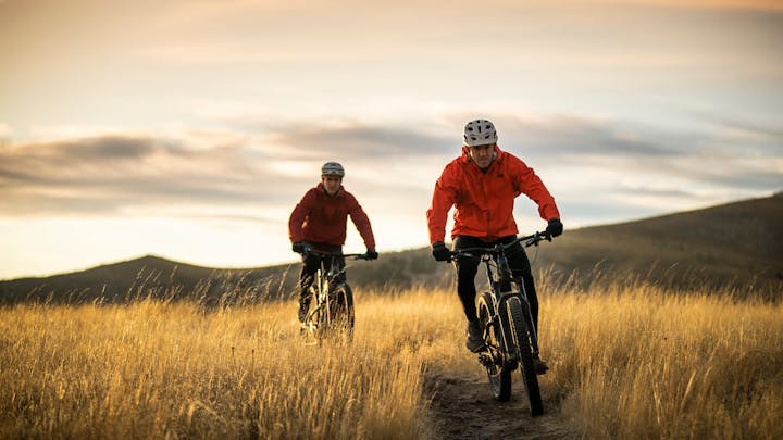 Two cyclists riding on a grassy trail at twilight.