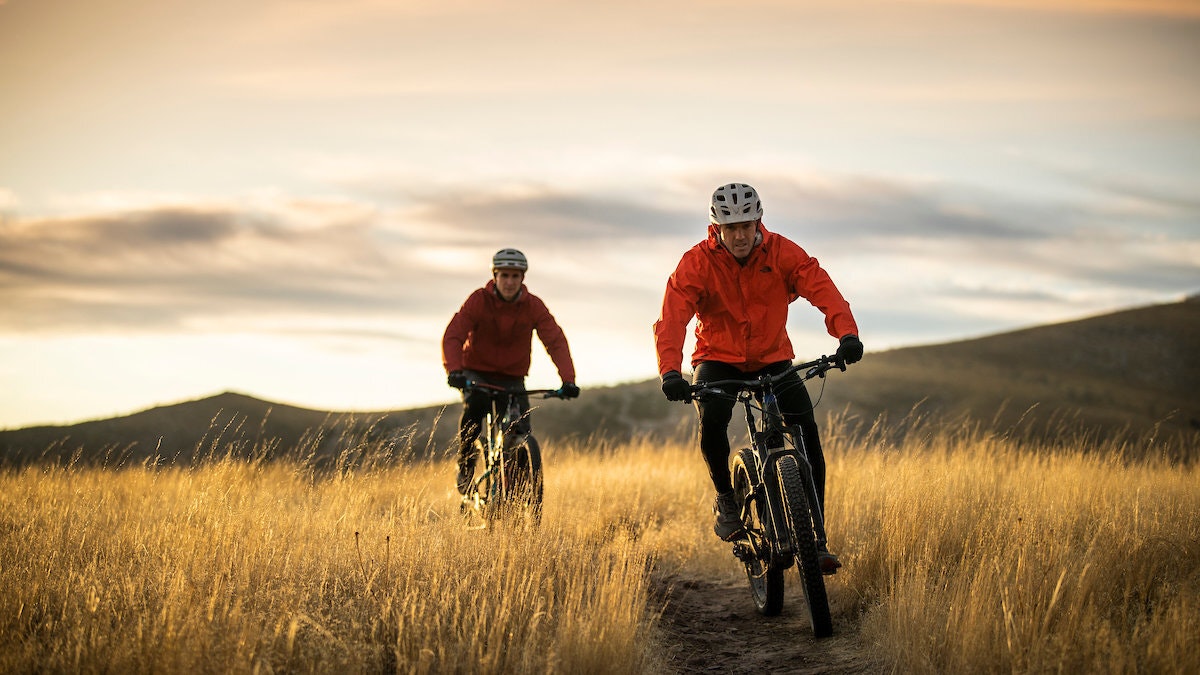 Two cyclists riding on a grassy trail at twilight.