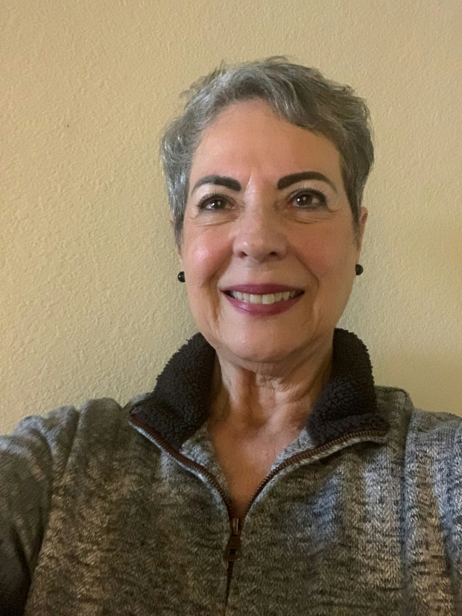 A smiling person wearing a zip-up top against a plain wall.