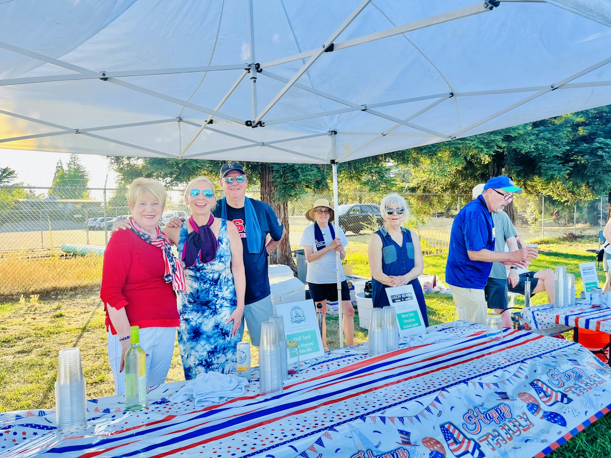 People at a festive outdoor event with a tent, table, and American-themed decorations.