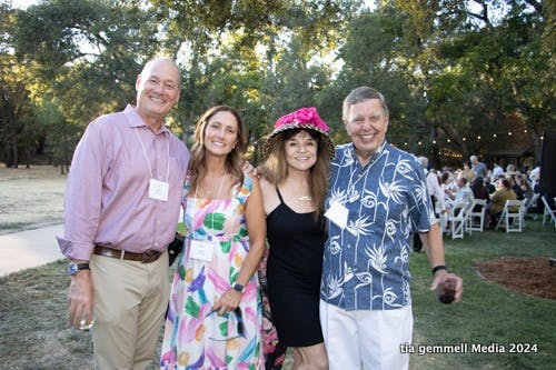Four people smiling outdoors at an event, wearing name tags.