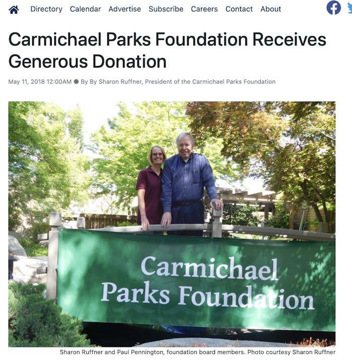 Two individuals stand behind a sign reading "Carmichael Parks Foundation" amidst a leafy backdrop.
