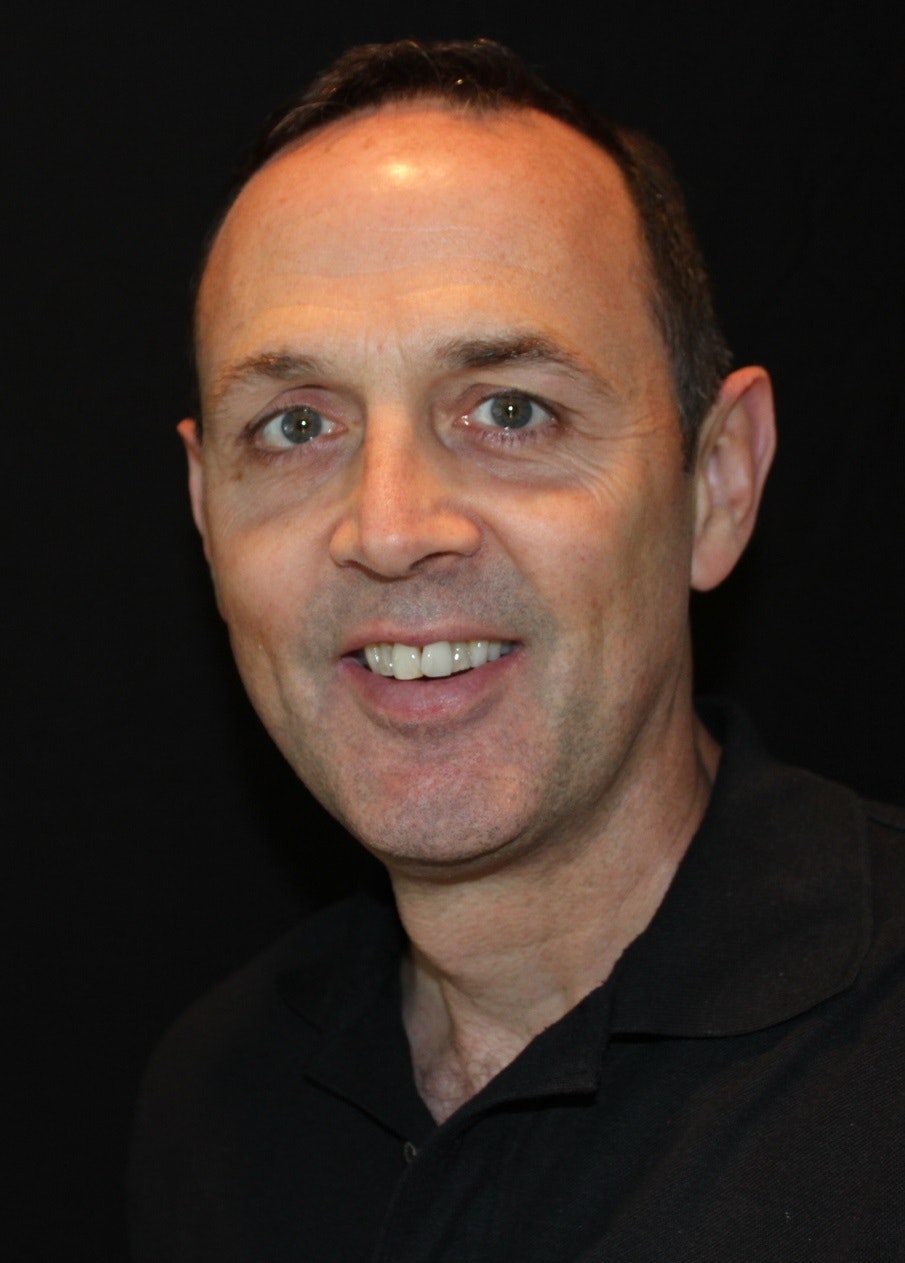 A smiling man in a black shirt against a black background.