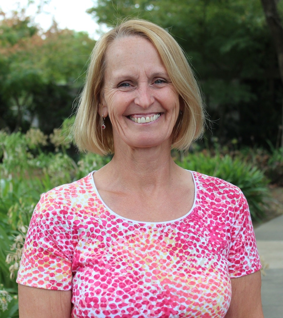 A smiling woman in a pink patterned shirt with a natural backdrop.