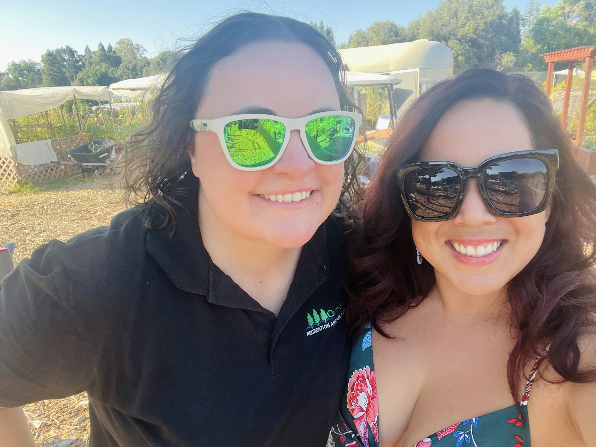 Two people wearing sunglasses smiling outdoors with a garden setting in the background.