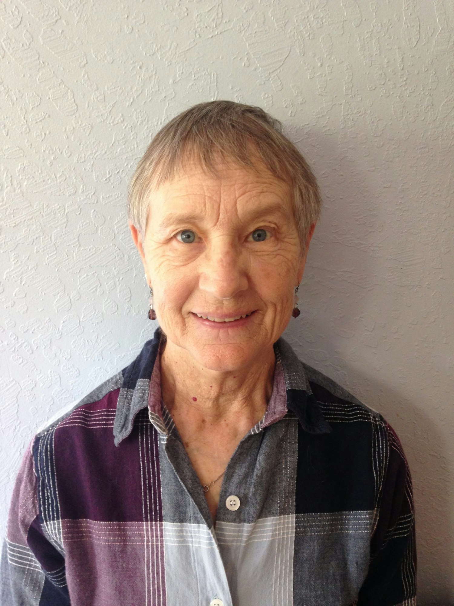 A smiling elderly woman with short hair wearing a striped shirt.