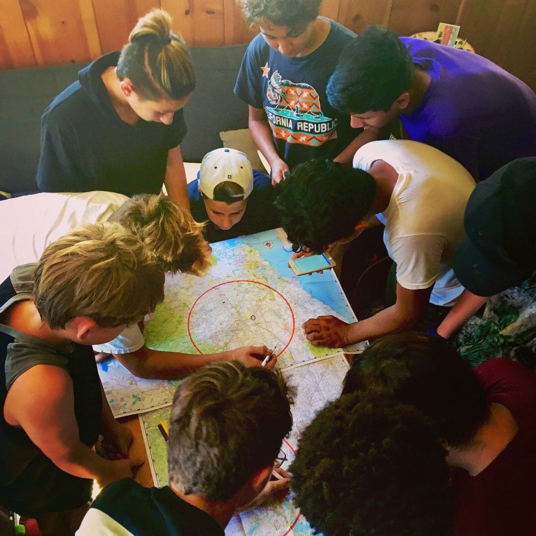 A group of people gathered around, looking at and discussing a map.