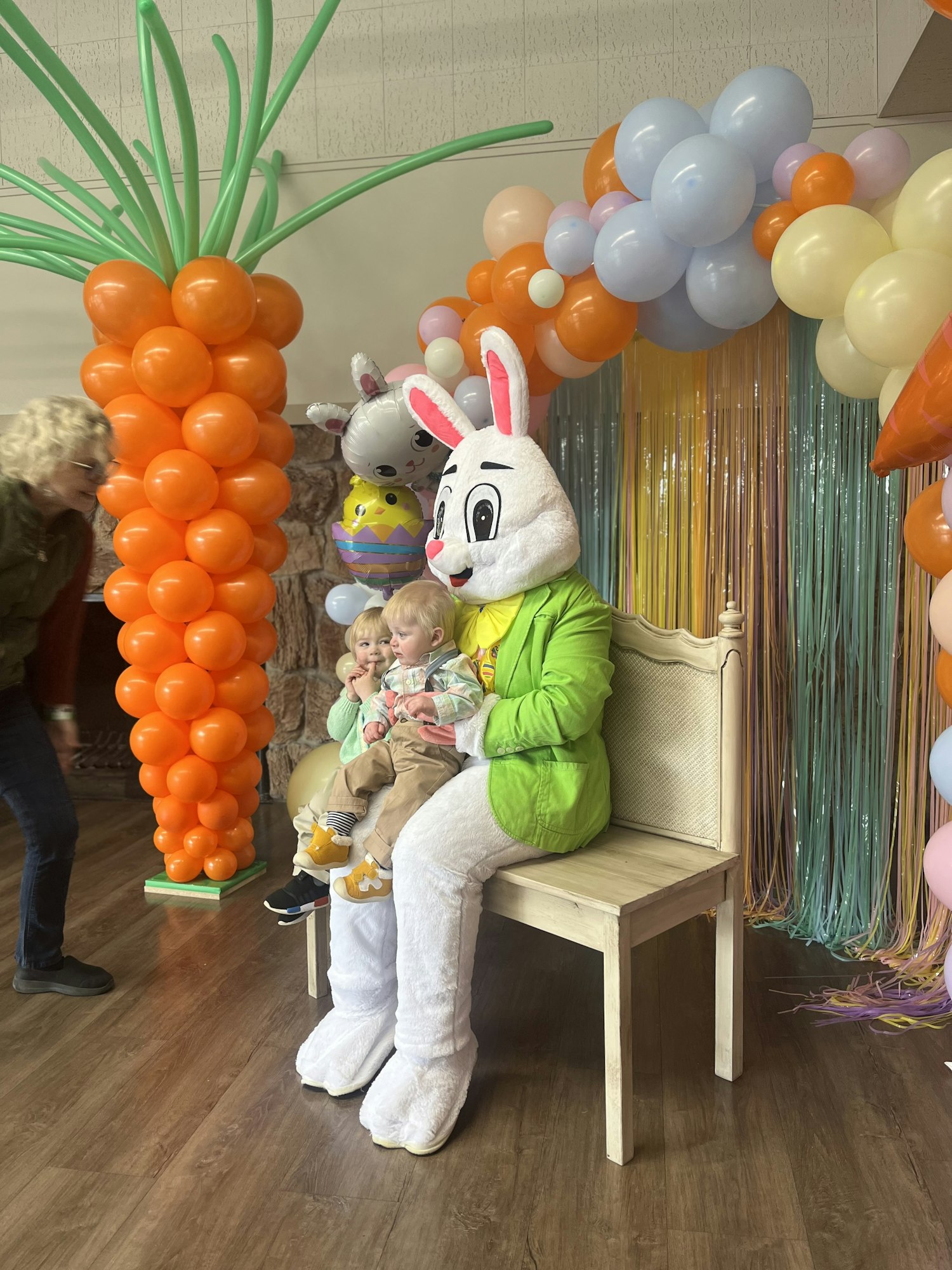 A person in a rabbit costume holding a child, with colorful balloon decorations around them.