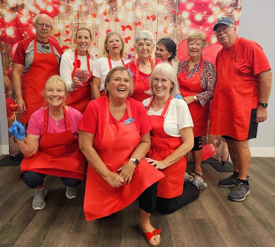 Group of happy people in red aprons, possibly volunteers or team members, festive background with hearts and lights.