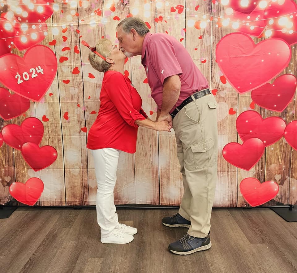 Two people sharing a kiss, surrounded by Valentine's Day decor with hearts and a "2024" sign.